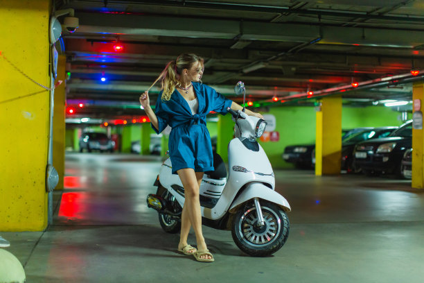 戴墨镜的金发女人坐在地下停车场的小摩托车旁。穿着蓝色套装的时装模特图片下载