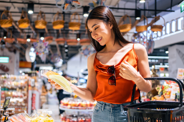 亚洲年轻漂亮的女人提着购物篮走进超市。有魅力的女孩感到快乐和放松，享受从购物部的货架上挑选商品。健康购物理念图片下载