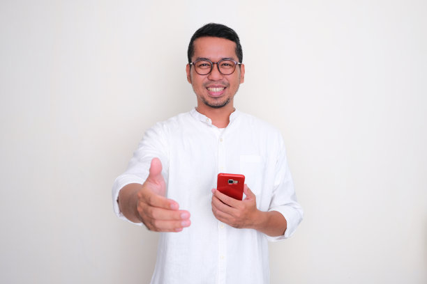 亚洲成年男子拿着手机微笑着和对方握手图片下载