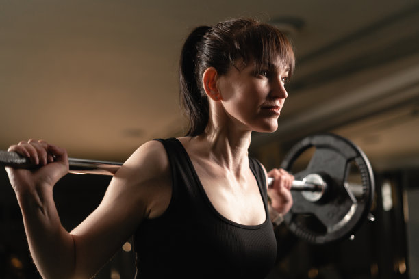 健身女性在健身房用大杠铃做运动。女性在做大杠铃运动时努力。图片下载