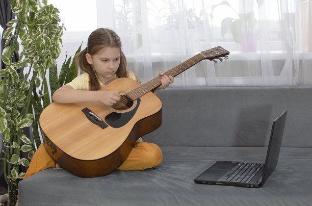 一个女孩在网上视频教程的帮助下，在公寓里学习弹木吉他图片下载