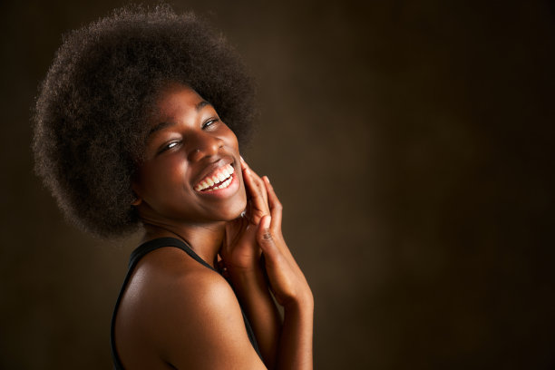 一个年轻的黑人妇女用手抚摸着她的脸，露出她完美的微笑图片下载