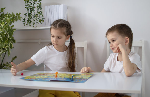 两个孩子在托儿所玩棋盘游戏“步行者”的照片。桌游与儿童休闲的概念。小朋友们在桌上用方块和筹码玩纸卡游戏图片下载