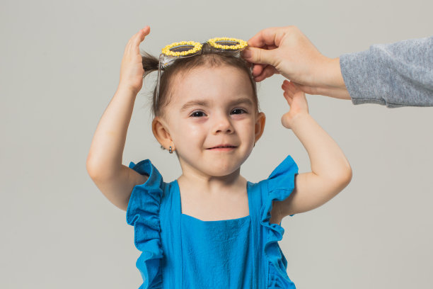 戴着太阳镜和蓝色西装的金发女婴在白色背景的工作室里。的孩子。的童年。发髻式。夏天的时尚图片下载