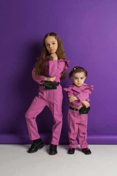 两个穿紫色衣服的金发女孩，背景是紫色的。的孩子。的童年。夏天的时尚图片下载