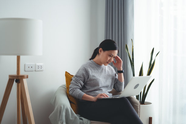 坐在家里客厅里使用笔记本电脑的亚洲妇女头痛不已。图片下载