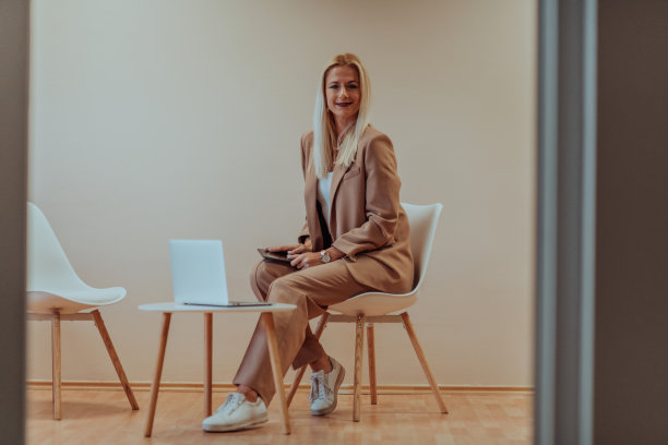 一位职业女商人坐在椅子上，周围是宁静的米色背景，她在笔记本电脑上勤奋地工作，展示了她追求成功的奉献精神和专注图片下载