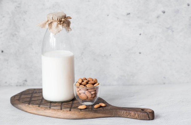 有机杏仁奶装在玻璃瓶里，旁边是放在石桌上的时髦木板上的杏仁。天然环保产品。图片下载