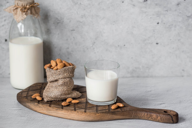 一个玻璃瓶里装着有机杏仁奶，旁边是一个装在袋子里的杏仁，放在石桌上一个时髦的木板上。天然环保产品。图片下载