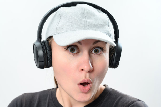 一个戴着无线耳机和帽子的女孩在白色背景上的肖像，复制空间与戴着耳机的女孩的情感照片。图片下载