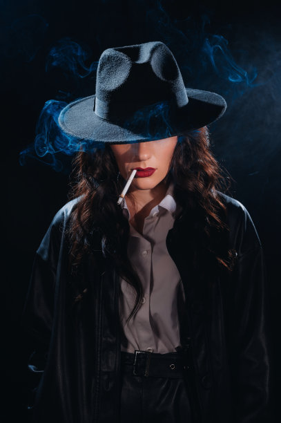 一个女侦探点燃香烟的黑色肖像。私家侦探、间谍、侦查概念。图片下载