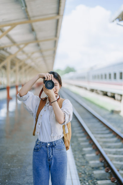 一名亚洲少女在车站等火车时，用相机拍照来捕捉记忆。图片下载