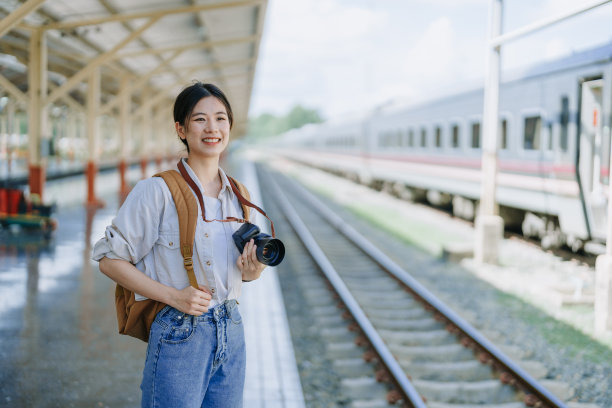 一名亚洲少女在车站等火车时，用相机拍照来捕捉记忆。图片下载