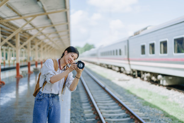 一名亚洲少女在车站等火车时，用相机拍照来捕捉记忆。图片下载