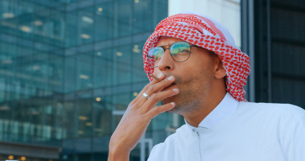 穆斯林，香烟和城市的一个商人在户外，在工作和工作之余抽着烟。伊斯兰教，成瘾和尼古丁烟雾与一名男性员工在宗教或文化的库菲图片下载