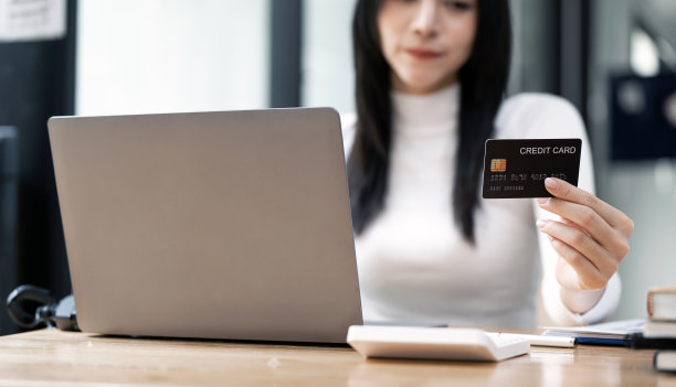 可爱的年轻女子拿着黑色信用卡，坐在共同工作的地方用电脑网购。图片下载
