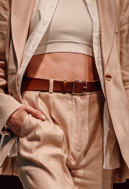 时髦的中性米色套装，优雅的夹克，露脐上衣，搭配棕色皮带的裤子。图片下载