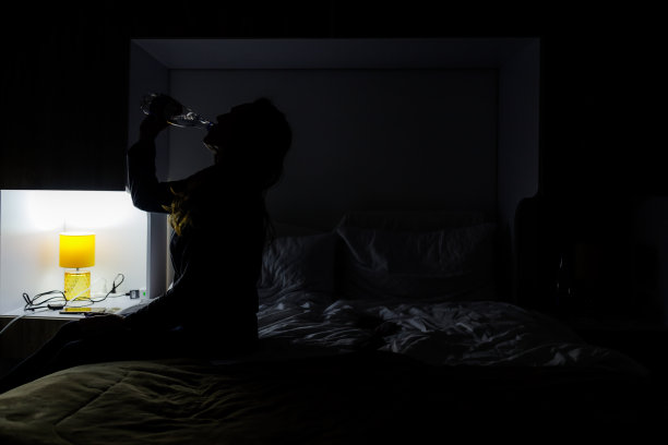 坐在床上的女人在半黑暗中喝水图片下载