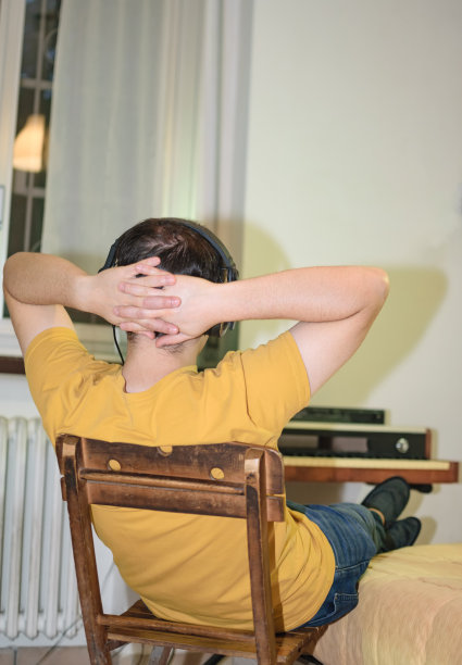 年轻人放松地把手臂放在脖子后面，戴着耳机听音乐图片下载