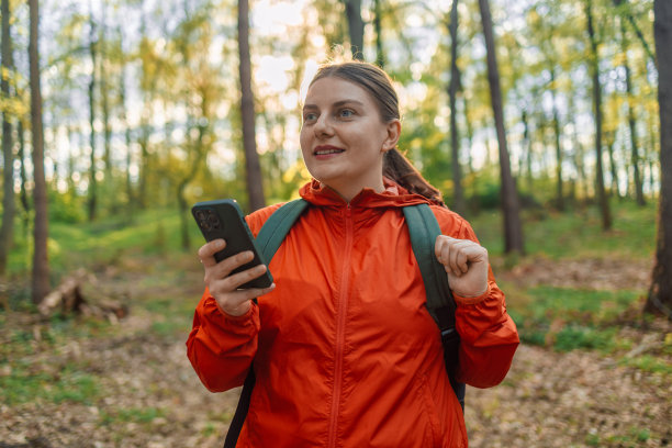 年轻的女旅行者背着背包，穿着暖和的衣服站在春天的森林里看着手机屏幕。徒步旅行的女人。森林里的木路。欧洲波兰的国家公园。高质量照片图片下载