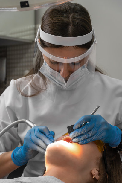 女牙医及助理正在清除牙齿上的牙石。到专业的牙科诊所就诊。女人坐在牙科椅上。钻牙治疗、补牙。细长立式照片图片下载