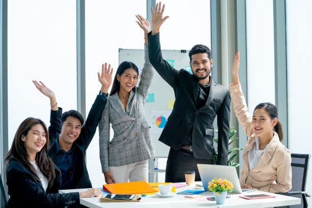 一群亚洲商人在办公室里举起双手，对项目的成功表示高兴和庆祝，他们也微笑着看着镜头。图片下载