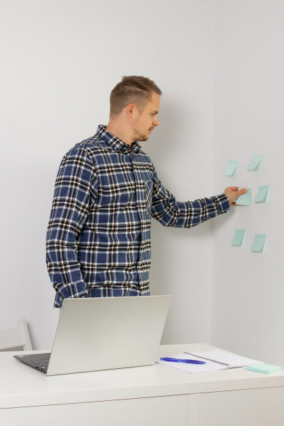 一个学生，一个专业的自由职业者看贴纸，看带有提醒的笔记。桌子上有一台笔记本电脑。照片图片下载