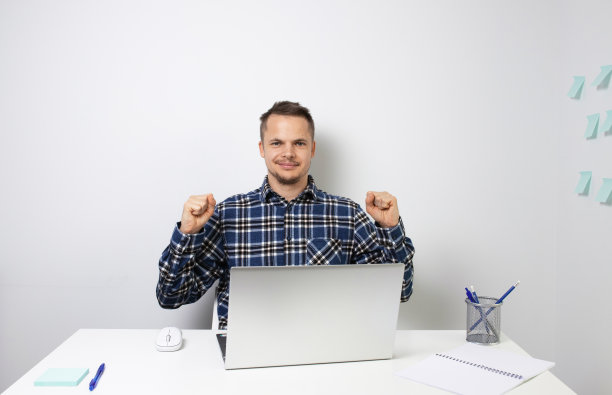 一个年轻人用笔记本电脑工作，微笑着，成功了。男人看着镜头。一个积极的人。照片。图片下载