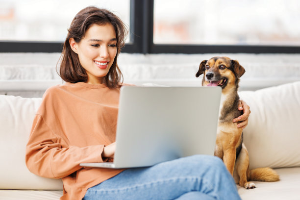 快乐的女性自由职业者在家里远程用笔记本电脑和宠物狗一起工作图片下载