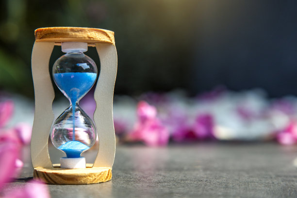 沙漏与蓝色的沙子在白色的石头和粉红色的夹竹桃花瓣自然背景。生命的时间，生命的意义和美的传递理念图片下载