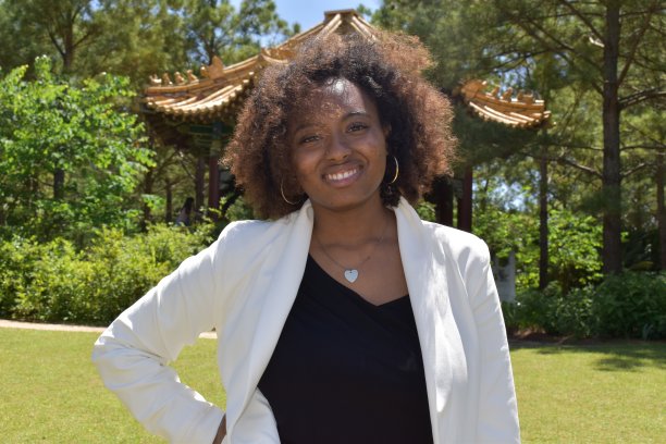 一个骄傲的有色女商人的肖像，穿着白色运动上衣，戴着心形吊坠。背景是日本花园。图片下载