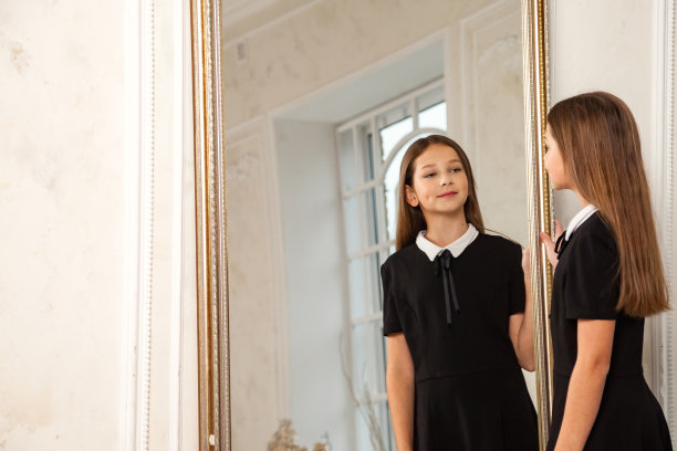 12岁的优雅少女在室内镜子前摆姿势，微笑着看着镜子。时尚可爱的青少年模特在时尚的黑色连衣裙的肖像。时尚青春的风格理念。复制广告文本空间图片下载