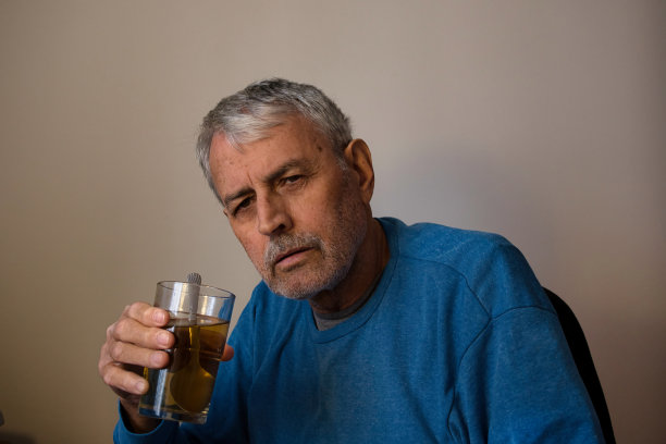 忧郁的老人端着一杯茶，心事重重。悲伤的成年人独自坐着，看着镜头。图片下载