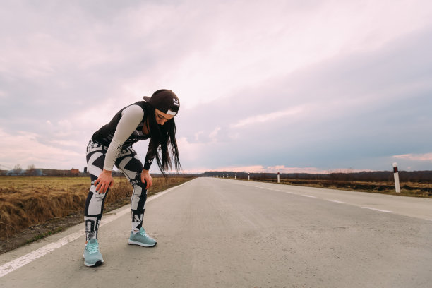 穿着运动服的女孩在空旷的道路上奔跑后呼吸图片下载