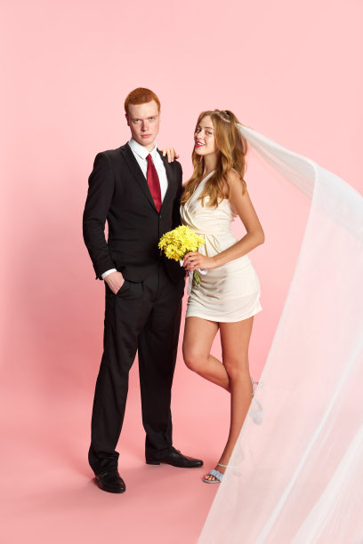 全家福。漂亮的年轻夫妇，男人和女人穿着西装和裙子结婚，在粉红色的工作室背景下摆姿势图片下载