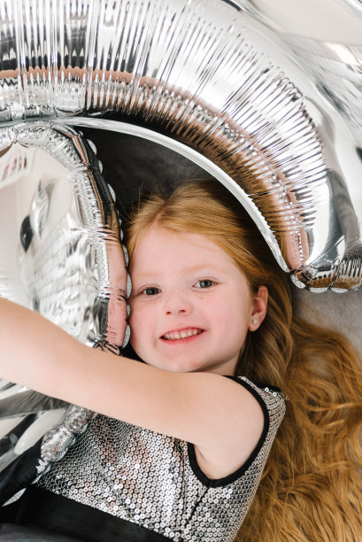 6年前女孩庆祝生日派对时很搞笑。照片墙，照片区装饰银色气球。庆祝活动的概念。生日宴会上的招待会。前视图。躺在地板上或床上。图片下载