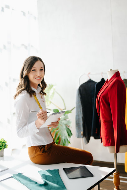 时装设计师女士在现代工作室里用智能手机和笔记本电脑与数码平板电脑交谈，衣服挂在架子上图片下载