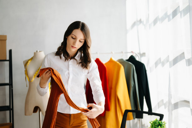 时装设计师女士在现代工作室里用智能手机和笔记本电脑与数码平板电脑交谈，衣服挂在架子上图片下载