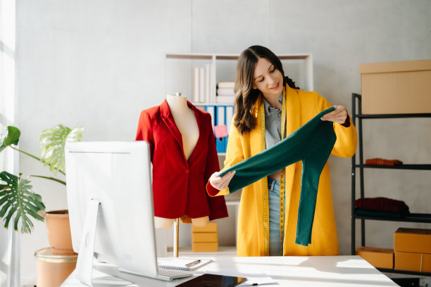 时装设计师女士在现代工作室里用智能手机和笔记本电脑与数码平板电脑交谈，衣服挂在架子上图片下载