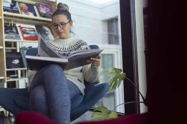 微笑的女学生坐在图书馆里，看书，翻书。冰岛图片下载