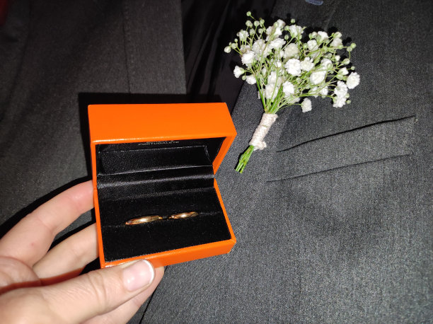婚礼上新郎的白色花胸花和一个装有新娘和新郎戒指的橙色盒子图片下载