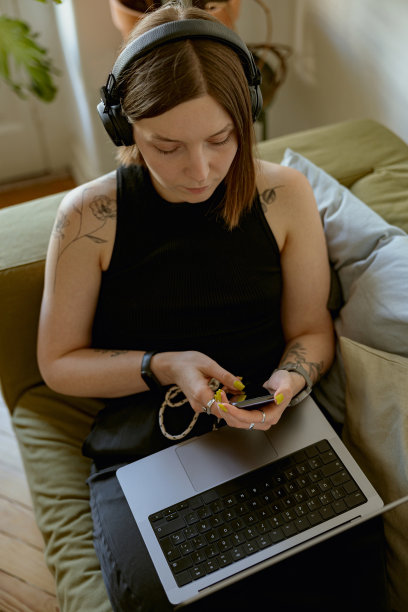 专注的女人坐在沙发上，使用智能手机和笔记本电脑，而在家办公室工作图片下载