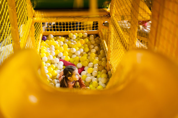 一个小女孩在黄色的游乐场里玩彩球。图片下载