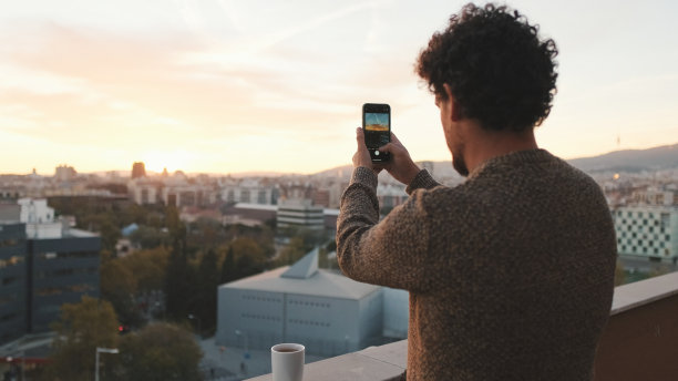 快乐的家伙在黎明时分站在阳台上，用智能手机拍照，拍摄美丽的景色图片下载