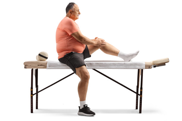 一位中年男人坐在按摩床上，手扶膝盖的全身照图片下载