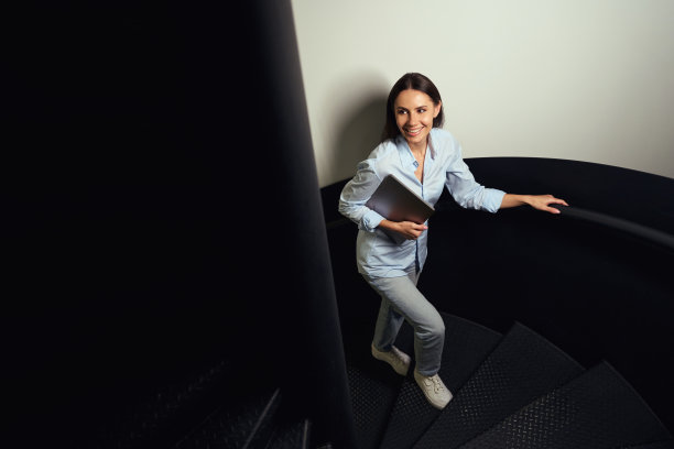 微笑的女人拿着笔记本电脑爬上螺旋楼梯图片下载