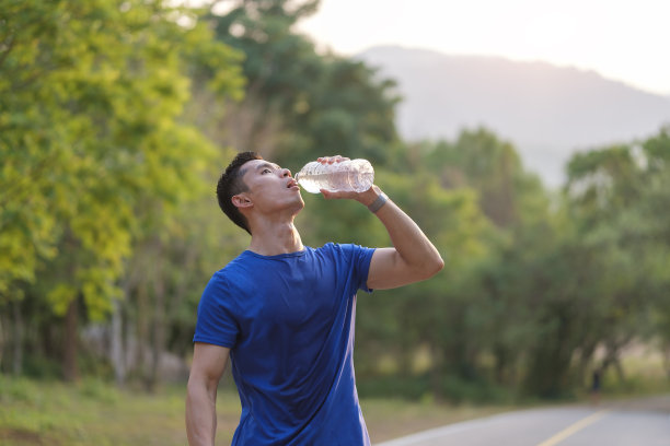 运动员在热带公园晨跑后用瓶子喝水。健康生活理念。图片下载