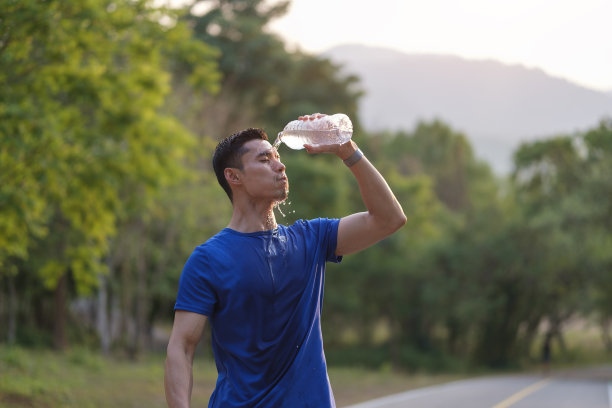运动员在热带公园晨跑后用瓶子喝水。健康生活理念。图片下载