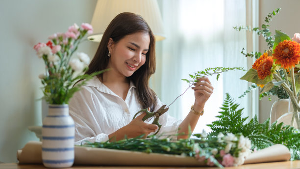 快乐的女花商正在剪植物的茎，在她的店里准备一束花。小企业的概念。图片下载