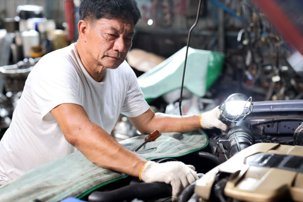 一名技术员，一名汽车修理工，穿着半制服，在维修站检查、保养汽车。工人拿着扳手和修理损坏的车辆。汽车中心维修服务理念。图片下载